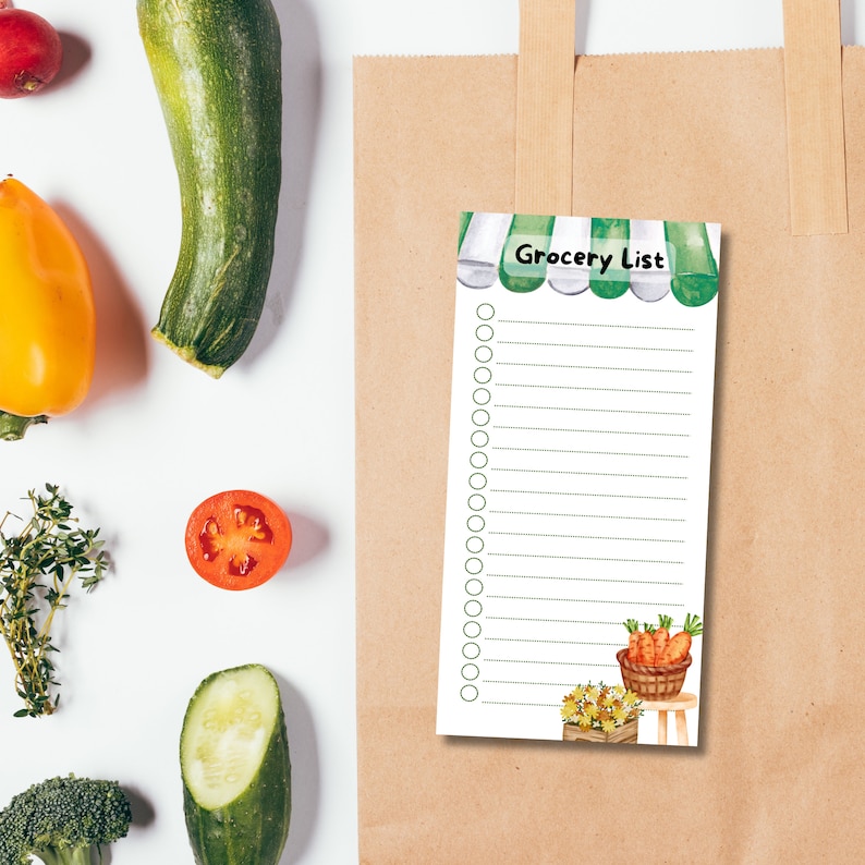 May include: A white grocery list notepad with a green awning and a basket of carrots. The notepad has a green border and a white background with lines for writing. The notepad is on a brown paper bag.