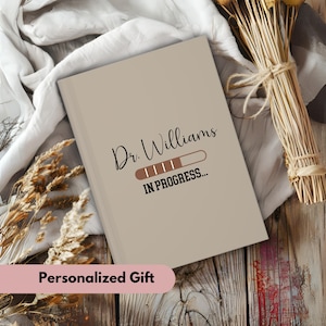 Pode incluir: Um caderno personalizado com uma capa bege e o texto "Dr. Williams IN PROGRESS..." com um gr&aacute;fico de barra de progresso.