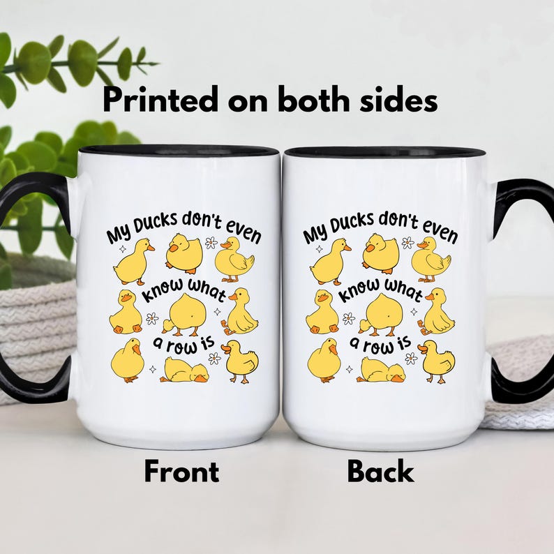 May include: White ceramic mug with a black handle and rim, featuring a design of yellow cartoon ducks. The front and back of the mug have the text "My Ducks don't even know what a row is". The mug is printed on both sides.