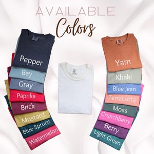May include: A display of folded t-shirts in various colors, including pepper, bay, gray, paprika, brick, mustard, blue spruce, and watermelon. The text "AVAILABLE Colors" is at the top. A white t-shirt is in the center.