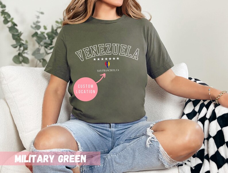 May include: Military green t-shirt with the word "VENEZUELA" in white, arched text above a small graphic of the Venezuelan flag and the text "SAN FRANCISCO, CA". The shirt is a solid color and has a crew neck.