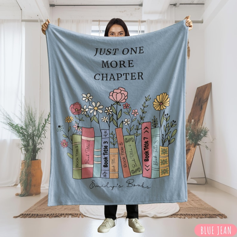 May include: A blue jean colored blanket with the text "JUST ONE MORE CHAPTER" and a floral and book design. The design includes colorful books, flowers, and the text "Emily's Books".