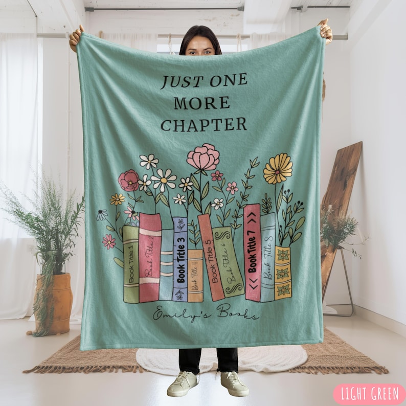 May include: A light green blanket with the text "JUST ONE MORE CHAPTER" and "Emily's Books". The blanket features a design of colorful books with flowers. The blanket is a soft, cozy throw.