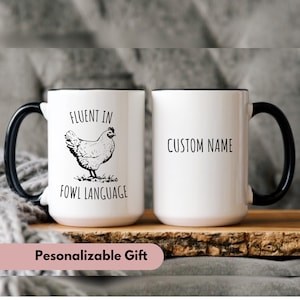 May include: White ceramic mug with a black handle and rim. The mug has a black and white illustration of a chicken and the text "Fluent in Fowl Language". The other side of the mug has the text "Custom Name".