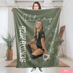 May include: A moss green blanket with the name "Valery" in white script and the text "SENIOR 2026" in white block letters. The blanket features a photo of a young woman in a soccer uniform holding a soccer ball. White star graphics are scattered across the blanket.