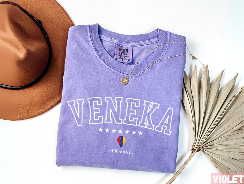 May include: Purple t-shirt with the word "Veneka" in white outlined letters, with a star design and the text "Chicago, IL" below. The shirt is made by "Comfort Colors".