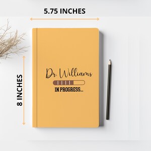Pode incluir: Um caderno amarelo com o texto "Dr. Williams" e uma barra de progresso que diz "IN PROGRESS..." O caderno mede 14,6 cm de largura e 20,3 cm de altura.
