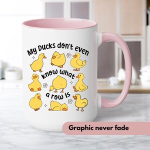 May include: White ceramic mug with a pink interior and handle. The mug features the text "My Ducks don't even know what a row is" and illustrations of yellow ducklings. The bottom of the mug has the text "Graphic never fade".