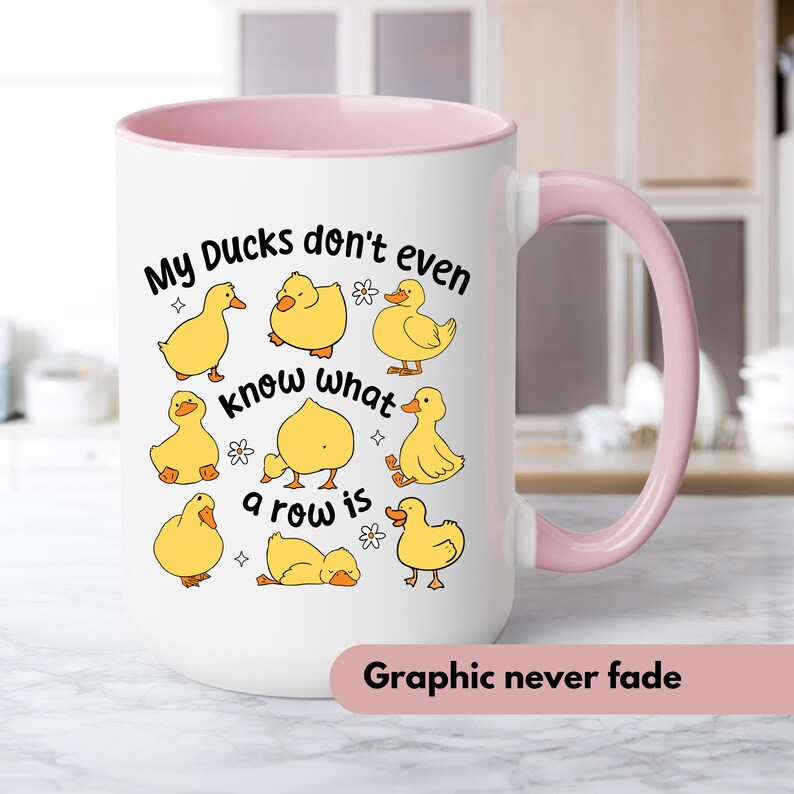 May include: White ceramic mug with a pink interior and handle. The mug features the text "My Ducks don't even know what a row is" and illustrations of yellow ducklings. The bottom of the mug has the text "Graphic never fade".