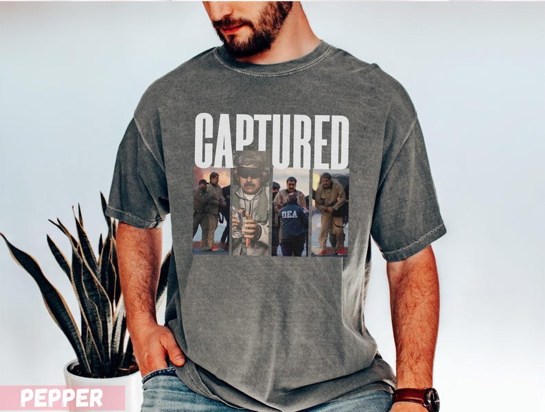 May include: A gray t-shirt with the word "CAPTURED" in white block letters. Below the text are three images of people. The shirt has a vintage, washed look. The person in the image is wearing a watch.