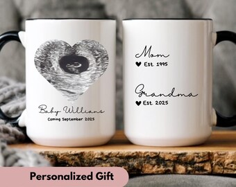May include: Two white ceramic mugs with black handles. The mug on the left has a black and white ultrasound image of a baby in a heart shape. The text below the image reads "Baby Williams Coming September 2025". The mug on the right has the text "Mom Est. 1995" and "Grandma Est. 2025". The text "Personalized Gift" is at the bottom of the image.