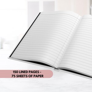 Pode incluir: Um caderno branco com uma lombada preta, aberto para revelar 150 p&aacute;ginas pautadas, ou 75 folhas de papel. O caderno est&aacute; sobre uma superf&iacute;cie branca.