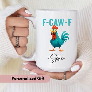 May include: White ceramic mug with a teal rooster illustration and the text "F-CAW-F". The mug also features the name "Steve" in a handwritten font. The words "Personalized Gift" are at the bottom.
