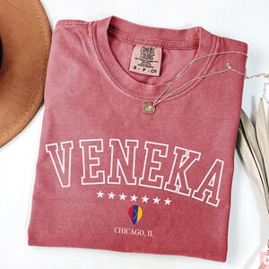 May include: A red t-shirt with the word "Veneka" in white outlined letters. The shirt has a small star design and the words "Chicago, IL" printed on the bottom.