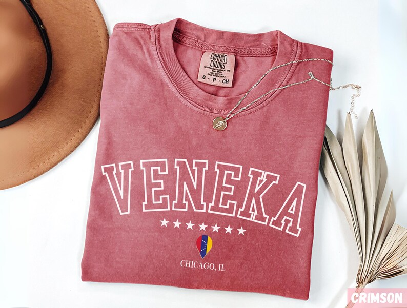 May include: A red t-shirt with the word "Veneka" in white outlined letters. The shirt has a small star design and the words "Chicago, IL" printed on the bottom.