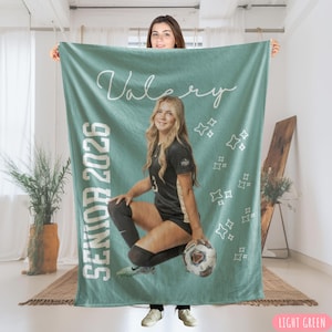 May include: A light green blanket featuring a photo of a young woman in a soccer uniform, holding a soccer ball. The blanket has the name "Valery" and "Senior 2026" printed on it, along with star graphics. The blanket is light green.