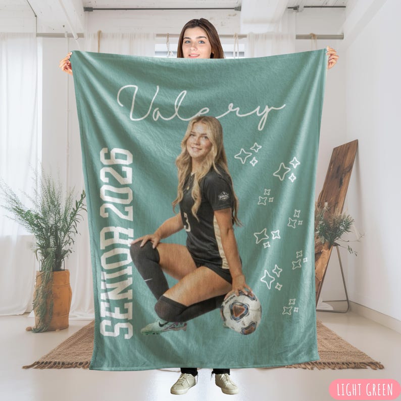 May include: A light green blanket featuring a photo of a young woman in a soccer uniform, holding a soccer ball. The blanket has the name "Valery" and "Senior 2026" printed on it, along with star graphics. The blanket is light green.