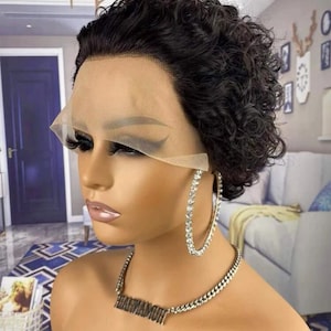 May include: A short, curly, black wig with a lace front. The wig is styled in a pixie cut and has a natural, wavy texture. The wig is on a mannequin head with a light brown skin tone. The mannequin is wearing a silver chain necklace with a nameplate pendant and large silver hoop earrings.