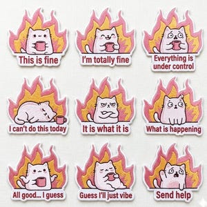 以下が含まれることがあります： 様々なポーズの白い猫が描かれた9つの刺繍パッチのコレクション。それぞれが様式化された炎に囲まれています。「This is fine」や「Send help」など、各パッチには異なるフレーズが書かれています。