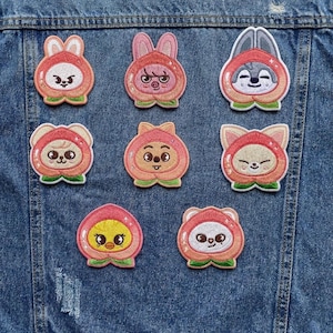 May include: Nine embroidered patches featuring cartoon characters in peach-shaped costumes. The patches have pink, orange, white, and green colors. The characters include a rabbit, pig, wolf, bear, fox, and a chick. The patches are on a denim jacket.