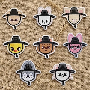 May include: A collection of nine embroidered patches featuring cartoon animal faces wearing black hats. The patches have a white border and are set against a tan fabric background. Each patch has a unique animal face design.