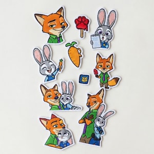Puede incluir: Parches bordados con personajes de la película animada Zootrópolis. Los parches representan un zorro y un conejo en varias poses, junto con una zanahoria, un helado con forma de pata y una placa de policía. Los parches son coloridos y detallados.