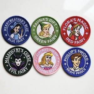 May include: Set of six embroidered patches featuring characters from a fairy tale. Each patch is round with a different color border and character illustration. Text includes "Merryweather's Blue", "Fauna's Gift", "Flora's Magic", "Maleficent's Curse", "Aurora's Dream", and "Phillip's Sword".