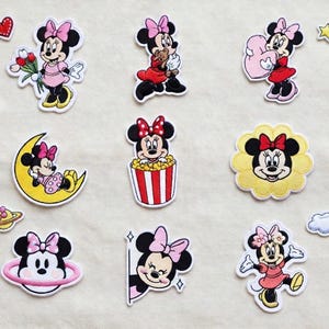 Può includere: Una collezione di toppe ricamate di Minnie Mouse in varie pose. Le toppe raffigurano Minnie Mouse con il suo fiocco distintivo, vestita con abiti diversi e circondata da cuori, stelle e fiori. Le toppe sono colorate e dettagliate.