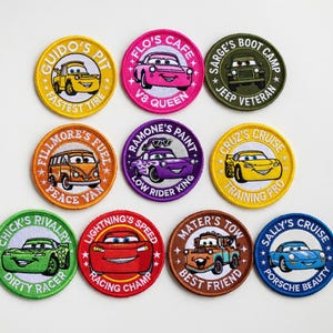 Könnte beinhalten: Neun aufgestickte Aufnäher mit Charakteren und Sätzen aus dem Film Cars. Die runden Aufnäher haben verschiedene Farben und Designs, darunter Autos und Texte wie "Guido's Pit" und "Lightning's Speed".