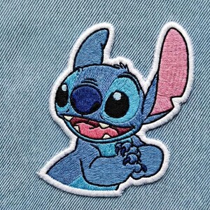 May include: Embroidered patch of the character Stitch from Lilo & Stitch. The patch features Stitch in blue, with pink inner ears and a white border. The patch is set against a light blue denim background.