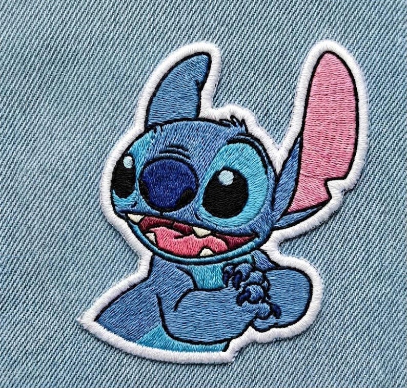 May include: Embroidered patch of the character Stitch from Lilo & Stitch. The patch features Stitch in blue, with pink inner ears and a white border. The patch is set against a light blue denim background.