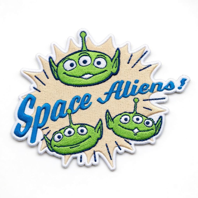 May include: Embroidered patch featuring three green aliens with three eyes each, set against a tan burst design. The patch reads "Space Aliens!" in blue lettering with a white border. The patch is on a white background.