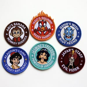Puede incluir: Conjunto de seis parches bordados con personajes y frases de la película de animación Aladdin. Los diseños incluyen a Abu el mono, Iago el loro, Genio, Jasmine, Jafar y Aladdin. Cada parche es circular con detalles coloridos y texto.