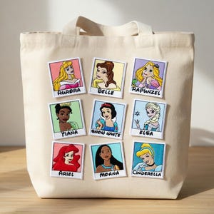 May include: Beige canvas tote bag with nine embroidered patches featuring Disney princesses: Aurora, Belle, Rapunzel, Tiana, Snow White, Elsa, Ariel, Moana, and Cinderella. The patches are rectangular with white borders.