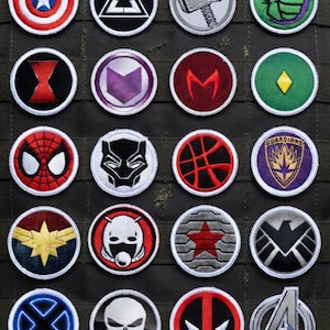 Pode incluir: Uma coleção de patches bordados com vários símbolos de super-heróis. Os patches redondos, com bordas brancas, retratam personagens como Capitão América, Homem-Aranha e o logotipo dos Vingadores. As cores incluem vermelho, azul, verde e preto.