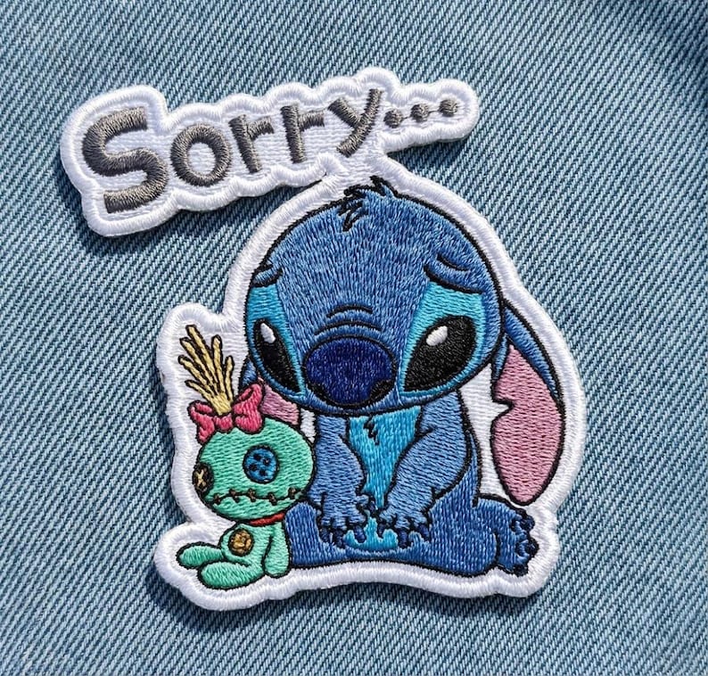 May include: Embroidered patch featuring the character Stitch from Lilo & Stitch, in shades of blue, with a sad expression. A small green doll with a pink bow is next to Stitch. The word "Sorry..." is embroidered above.