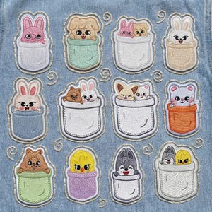 May include: A collection of twelve embroidered patches featuring various cartoon animals, including bunnies, dogs, cats, and a bear, peeking out of pocket-shaped designs. The patches are in pastel colors and are sewn onto a light blue denim fabric.