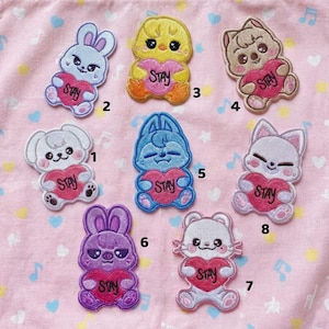 May include: Embroidered patches featuring various cartoon animals, including a bunny, chick, cat, and bear, each holding a heart with the word "STAY." The patches are in shades of blue, purple, yellow, and brown, with pink hearts.