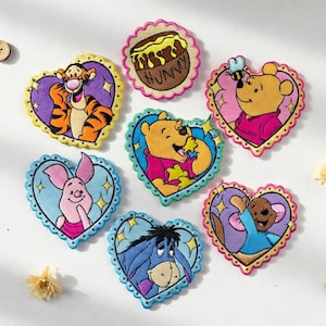 Puede incluir: Parches bordados con personajes queridos de Winnie the Pooh. Los parches tienen forma de corazón y circular con bordes festoneados. Los personajes incluyen Tigger, Pooh, Piglet, Eeyore y Roo. Los parches son coloridos.