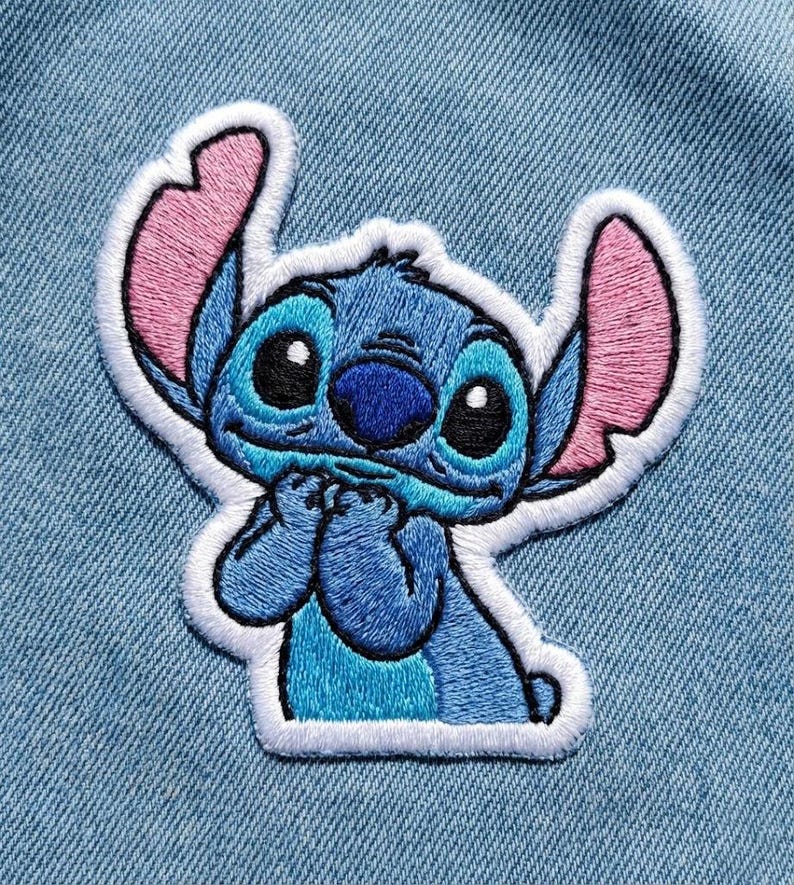 May include: Embroidered patch of the character Stitch from Lilo & Stitch. The patch is blue with pink ears, black eyes, and a white border. The character is in a pose with its hands clasped together.