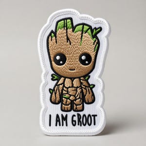 Puede incluir: Parche bordado con un personaje de dibujos animados que se asemeja a un árbol. El personaje es marrón con detalles verdes y grandes ojos negros. El parche incluye el texto "I AM GROOT" en letras negras.