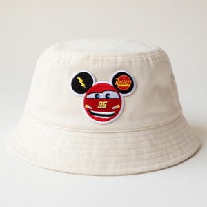 Puede incluir: Un juego de tres tazas de cer&aacute;mica con un esmalte moteado de color crema. Cada taza presenta un dise&ntilde;o pintado a mano diferente: una hoja azul y verde, una flor amarilla y una baya roja. Las tazas tienen una forma simple y redondeada.