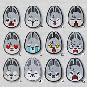 May include: A collection of twelve embroidered patches, each featuring a gray wolf-like character with different facial expressions. The patches have a light gray background and a dark gray border. The expressions range from happy to sad, with hearts, stars, and tears.