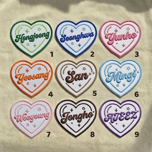 May include: Nine heart-shaped embroidered patches with names and the word "ATEEZ". Each patch has a different color border and name. The names include Hongjoong, Seonghwa, Yunho, Yeosang, San, Mingi, Wooyoung, Jongho, and ATEEZ.