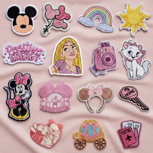 Puede incluir: Colección de parches bordados con personajes de dibujos animados, un arcoíris, un sol y las palabras "Positive Energy". Los parches incluyen Mickey Mouse, Minnie Mouse, Rapunzel y una cámara rosa.