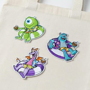 May include: Three embroidered patches featuring cartoon characters relaxing in inner tubes and holding coconut drinks. The characters include a green one-eyed monster, a blue monster, and a purple dragon, all wearing Hawaiian shirts.