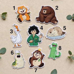 Könnte beinhalten: Eine Sammlung von acht aufgestickten Aufnähern mit verschiedenen Zeichentricktieren und -figuren. Enthält ein Eichhörnchen, einen Bären, eine Gans, einen Jungen, einen Otter, eine Raupe, einen Biber und einen Frosch. Jeder Aufnäher hat einen weißen Rand.