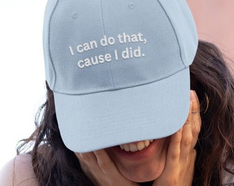 Puede incluir: Una mujer lleva una gorra de béisbol azul claro con el texto "I can do that, cause I did." La gorra está bordada con texto blanco. Lleva un top blanco sin mangas y pantalones vaqueros negros.
