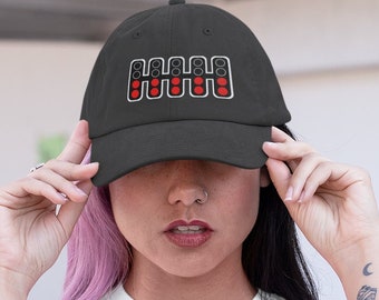 Puede incluir: Una mujer con una camiseta blanca con el texto "It's Lights Out and away we go" y una gorra de béisbol negra con un patrón de cambio de marchas rojo y blanco. Lleva pantalones vaqueros azules.