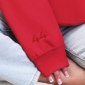 Op de afbeelding: Rood sweatshirt met een witte "44" gedrukt op de mouw.